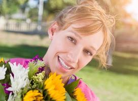 retrato al aire libre de una mujer de ojos marrones adulta joven emocionada que sostiene un ramo de flores. foto