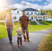 Happy Mixed Race Family Walking in Front of Beautiful Custom Home. photo