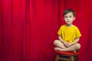 niño de raza mixta sentado en un taburete frente a la cortina foto