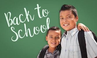 Hispanic Boys Wearing Backpacks In Front of Back To School Written On Chalk Board photo