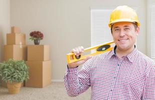 Male Construction Worker In Room With Moving Boxes Holding Level photo