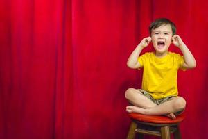 niño, dedos en los oídos en un taburete frente a la cortina foto