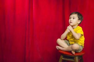 niño de raza mixta sentado en un taburete frente a la cortina foto
