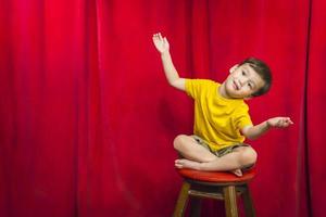 niño de raza mixta sentado en un taburete frente a la cortina foto