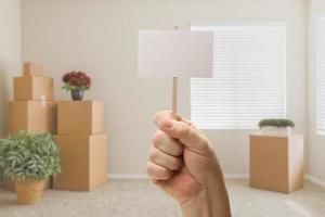 Hand Holding Blank Sign in Empty Room with Packed Moving Boxes photo