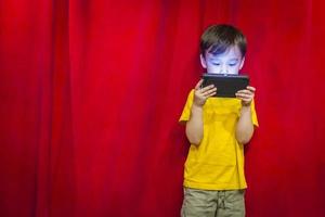 niño de raza mixta mirando el teléfono celular frente a la cortina foto