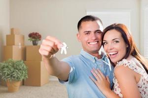 Young Military Couple with House Keys in Empty Room with Packed Moving and Potted Plants photo