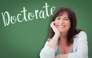 Doctorate Written On Green Chalkboard Behind Smiling Middle Aged Woman photo