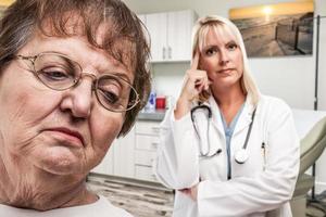 Empathetic Doctor Standing Behind Troubled Senior Adult Woman In Office photo