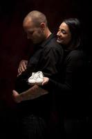 Mixed Race Couple Holding New White Baby Shoes on Black photo