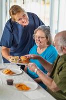 Female Doctor or Nurse Serving Senior Adult Couple Sandwiches at Table photo