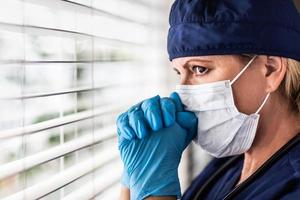 Stressed Female Doctor or Nurse On Break At Window Wearing Medical Face Mask photo