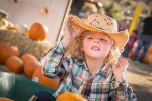 niño sentado con un sombrero de vaquero en un rancho rústico en el huerto de calabazas. foto