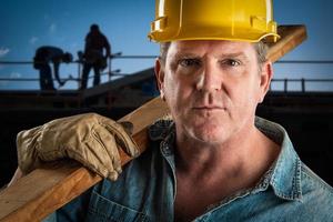 contratista serio con casco que lleva tablones de madera en el sitio de construcción. foto