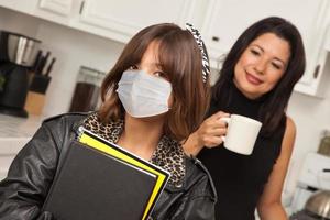 Young Hispanic Girl Student with Mother At Home Getting Ready For School Wearing Medical Face Mask photo