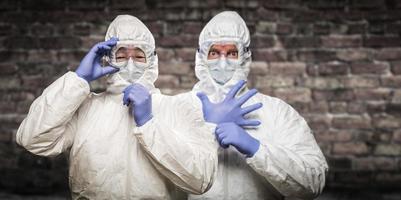 Chinese and Caucasian Men Wearing Hazmat Suit, Goggles and Mask with Brick Wall Background photo