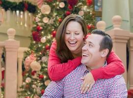 Caucasian Couple Laughing In Front of Decorated Christmas Tree. photo