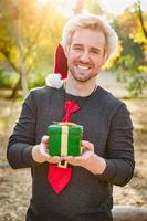 apuesto joven caucásico festivo sosteniendo un regalo de navidad al aire libre foto