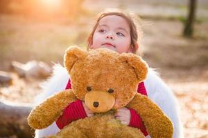 Cute Young Mixed Race Baby Girl Hugging Teddy Bear Outdoors photo