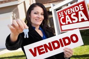 mujer hispana sosteniendo un cartel vendido frente al cartel y la casa de se vende casa foto