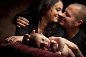 Una pareja de raza mixta mira amorosamente mientras el bebé se acuesta en la almohada foto
