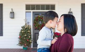 madre china y niño de raza mixta frotando la nariz de pie en el porche delantero decorado con navidad foto