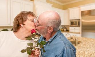 Happy Senior Adult Man Giving Red Rose to His Wife Inside Kitchen. photo