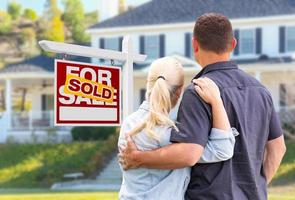 Young Adult Couple Facing Front of Sold Real Estate Sign and House photo