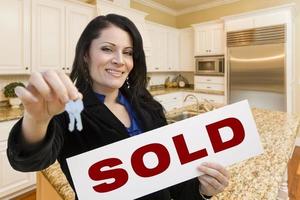 Hispanic Woman In Kitchen Holding House Keys and Sold Sign photo