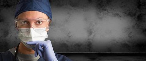 doctora o enfermera con gafas, guantes quirúrgicos y mascarilla facial contra una pancarta de fondo oscuro y sucio foto