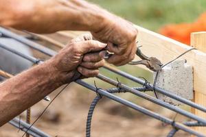 Worker Securing Steel Rebar Framing With Wire Plier Cutter Tool At Construction Site photo