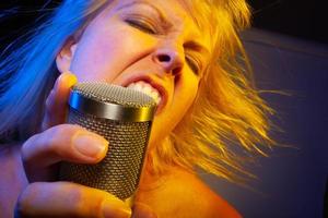 Female vocalist under gelled lighting sings with passion into condenser microphone. photo