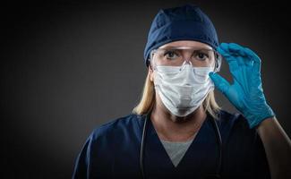 Female Medical Worker Wearing Protective Face Mask and Gear Against Dark Background photo