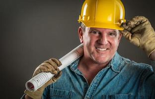 Smiling Contractor in Hard Hat Holding Floor Plans With Dramatic Lighting. photo