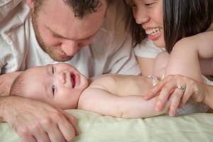 Bebé chino y caucásico de raza mixta acostado en la cama con sus padres foto