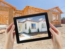 Female Hands Holding Computer Tablet with Finished House on Screen, Construction Framing Behind. photo
