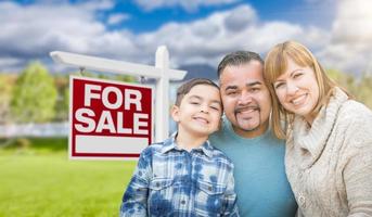 retrato de familia de raza mixta en frente de la casa y en venta signo de bienes raíces foto