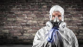 Woman Wearing Hazmat Suit, Protective Gas Mask and Goggles Against Brick Wall photo