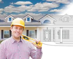 Male Contractor Wearing Hard Hat In Front of House Drawing Gradation Into Photograph. photo