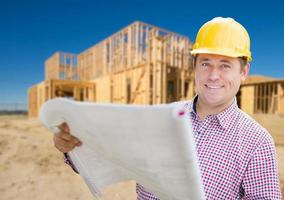 contratista sonriente con casco sosteniendo planos en el sitio de construcción de viviendas. foto