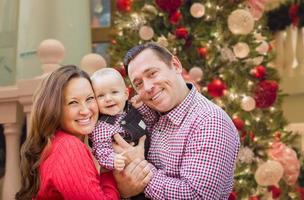 felices padres jóvenes con bebé frente al árbol de navidad decorado. foto