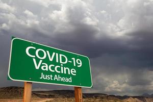 COVID-19 Coronavirus Vaccine Green Road Sign Against Ominous Stormy Cloudy Sky photo