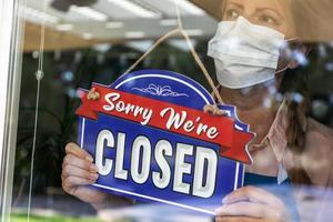 Female Store Owner Wearing Medical Face Mask Turning Sign to Closed in Window photo