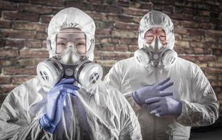 Chinese Woman and Man In Gas Masks, Goggles and Hazmat Suites Against Brick Background photo