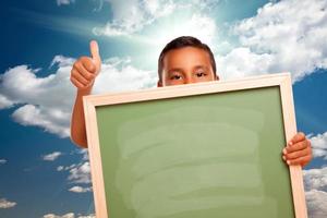 Proud Hispanic Boy Holding Blank Chalkboard Over Sky photo