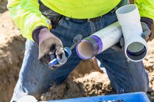 fontanero aplicando limpiador de tuberías, imprimación y pegamento a la tubería de pvc en el sitio de construcción foto