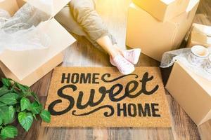 Woman Wearing Sweats Relaxing Near Home Sweet Home Welcome Mat, Moving Boxes and Plant. photo