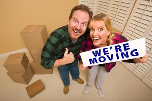 Goofy Couple Holding We're Moving Sign Surrounded by Boxes photo
