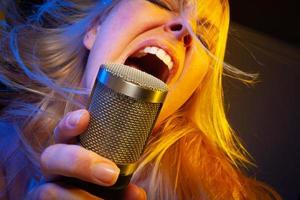 Female vocalist under gelled lighting sings with passion into condenser microphone. photo