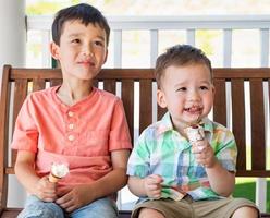 jóvenes hermanos chinos y caucásicos de raza mixta disfrutando de sus conos de helado foto